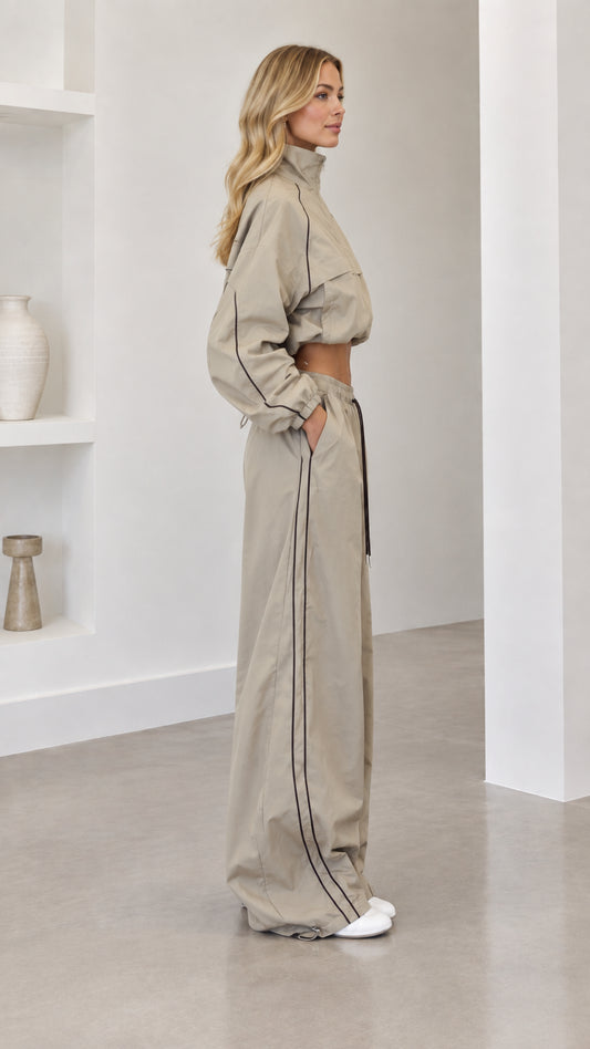 Side profile view of model wearing taupe two-piece windbreaker tracksuit set