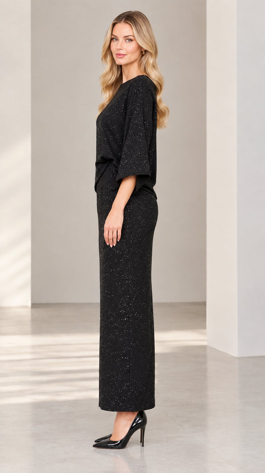 Side profile view of woman modeling black glitter two-piece maxi set with high heels