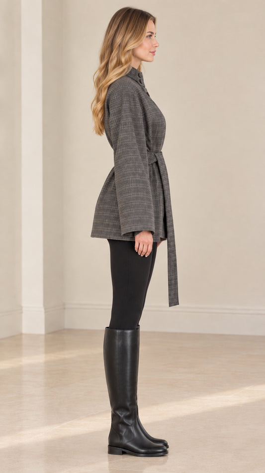 Side profile of woman wearing grey plaid belted jacket with knee-high black boots