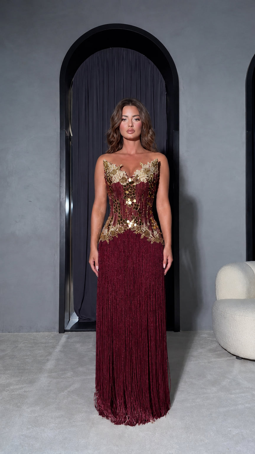 Front view of model wearing Burgundy strapless evening dress with gold embellished bodice and wine red fringe
