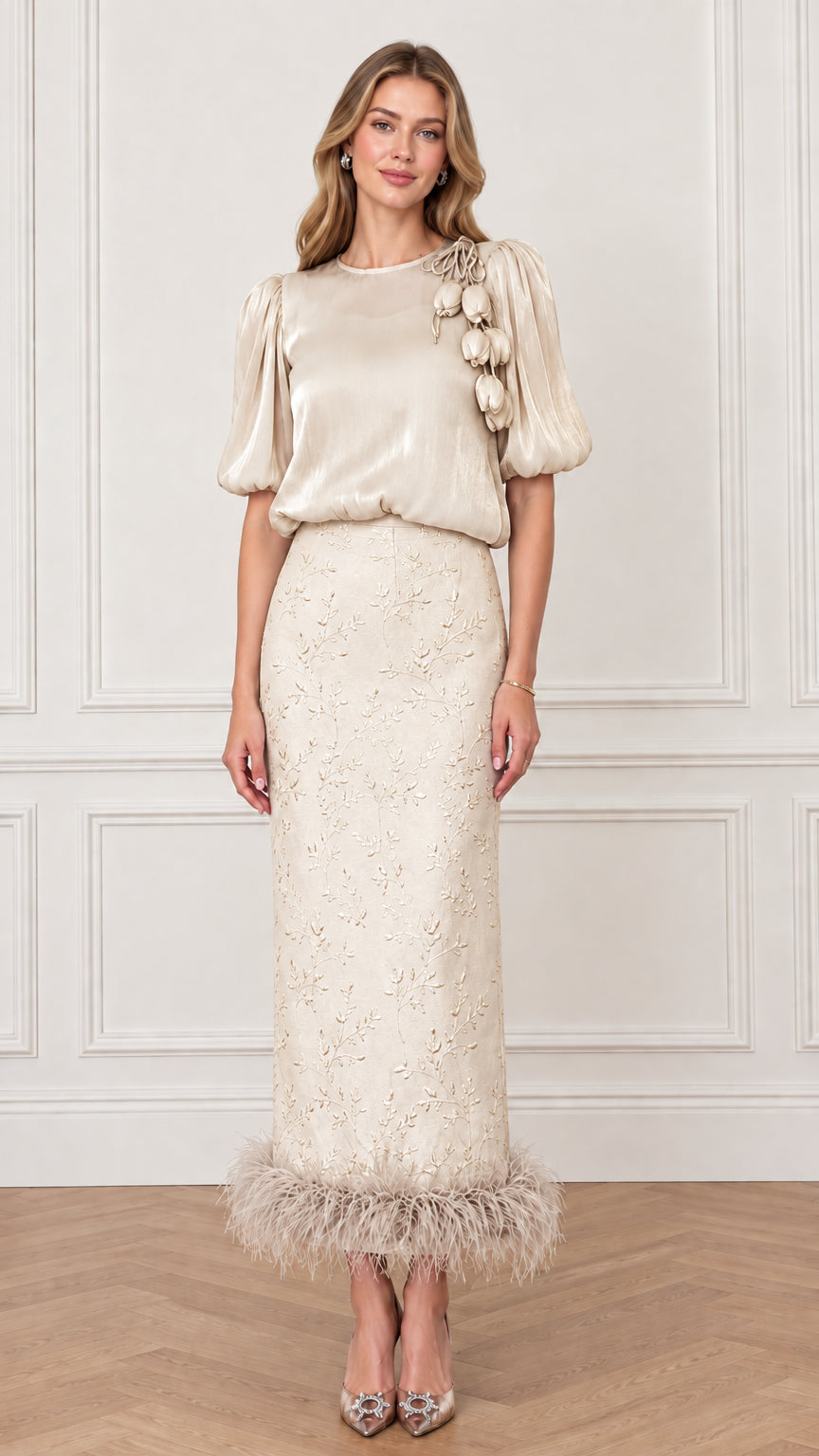 Model wearing Champagne gold puff sleeve top and embroidered column skirt with feather trim