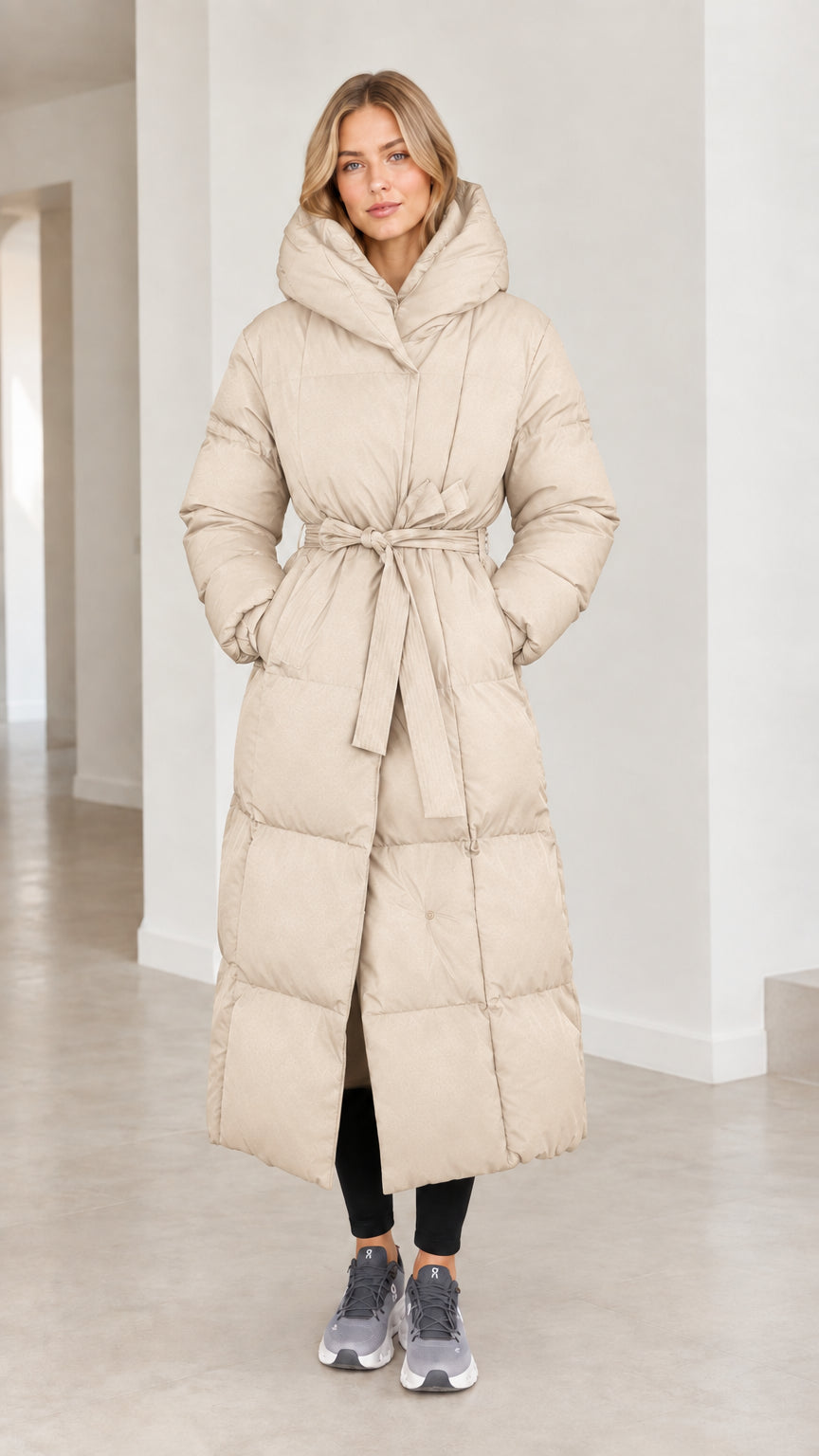 Front view of model wearing cream beige maxi hooded belted winter puffer coat