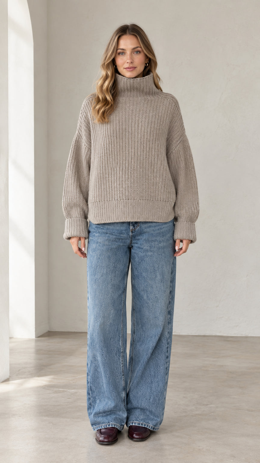 Front view of model wearing relaxed taupe chunky ribbed turtleneck sweater with wide leg jeans