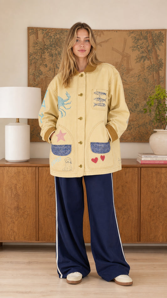 Front view of model wearing the butter yellow graphic barn jacket with corduroy collar and navy track pants