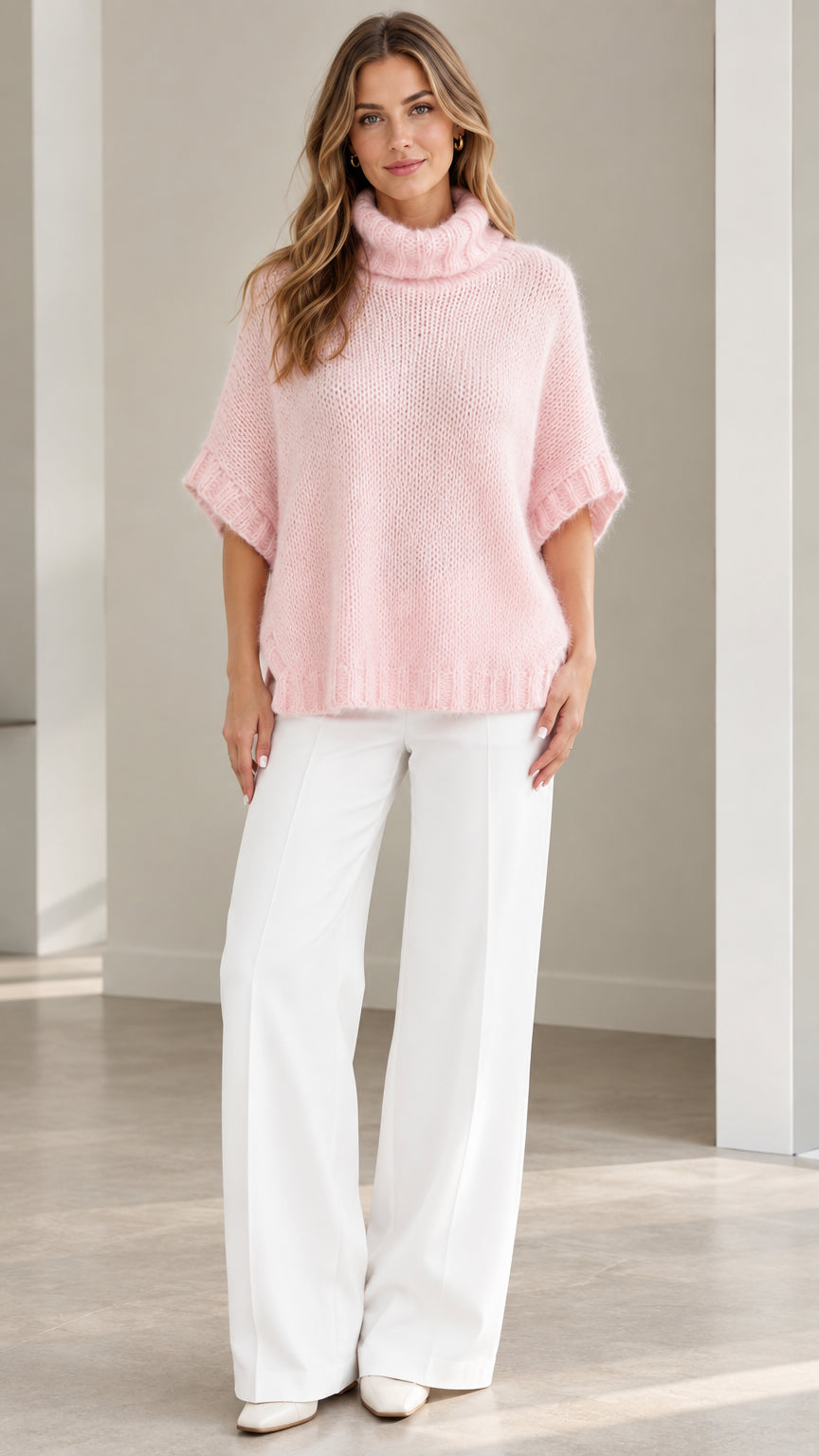 Front view of model wearing Light Pink short sleeve fuzzy turtleneck poncho sweater with white wide-leg trousers