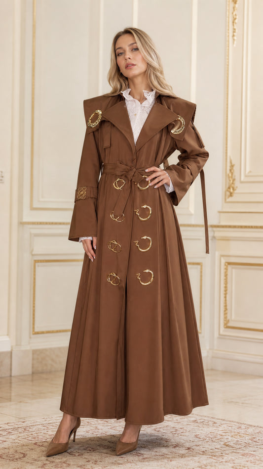 Full-length front view of woman wearing brown maxi belted trench coat with gold hardware