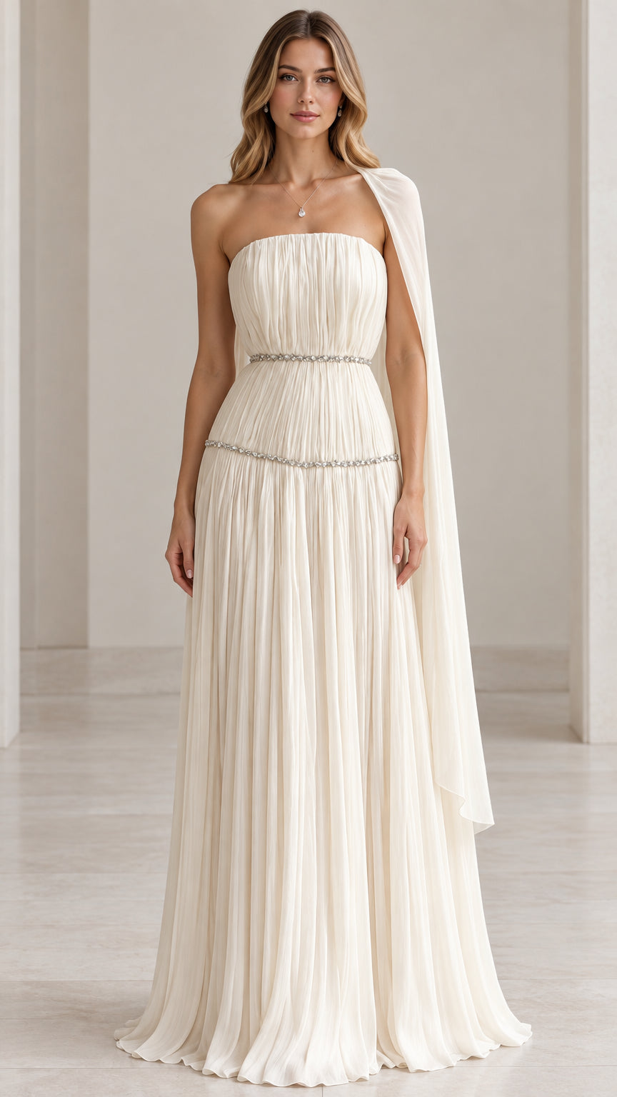 Front view of model wearing ivory strapless pleated evening gown with shoulder drape and crystal trim