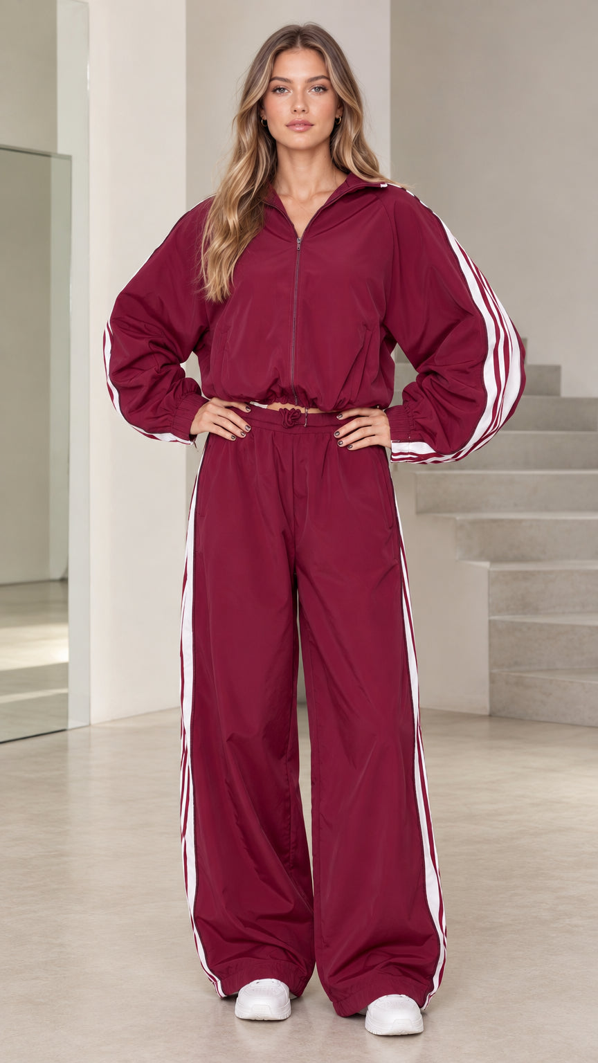 Front view of model wearing burgundy hooded windbreaker tracksuit set with white side stripes