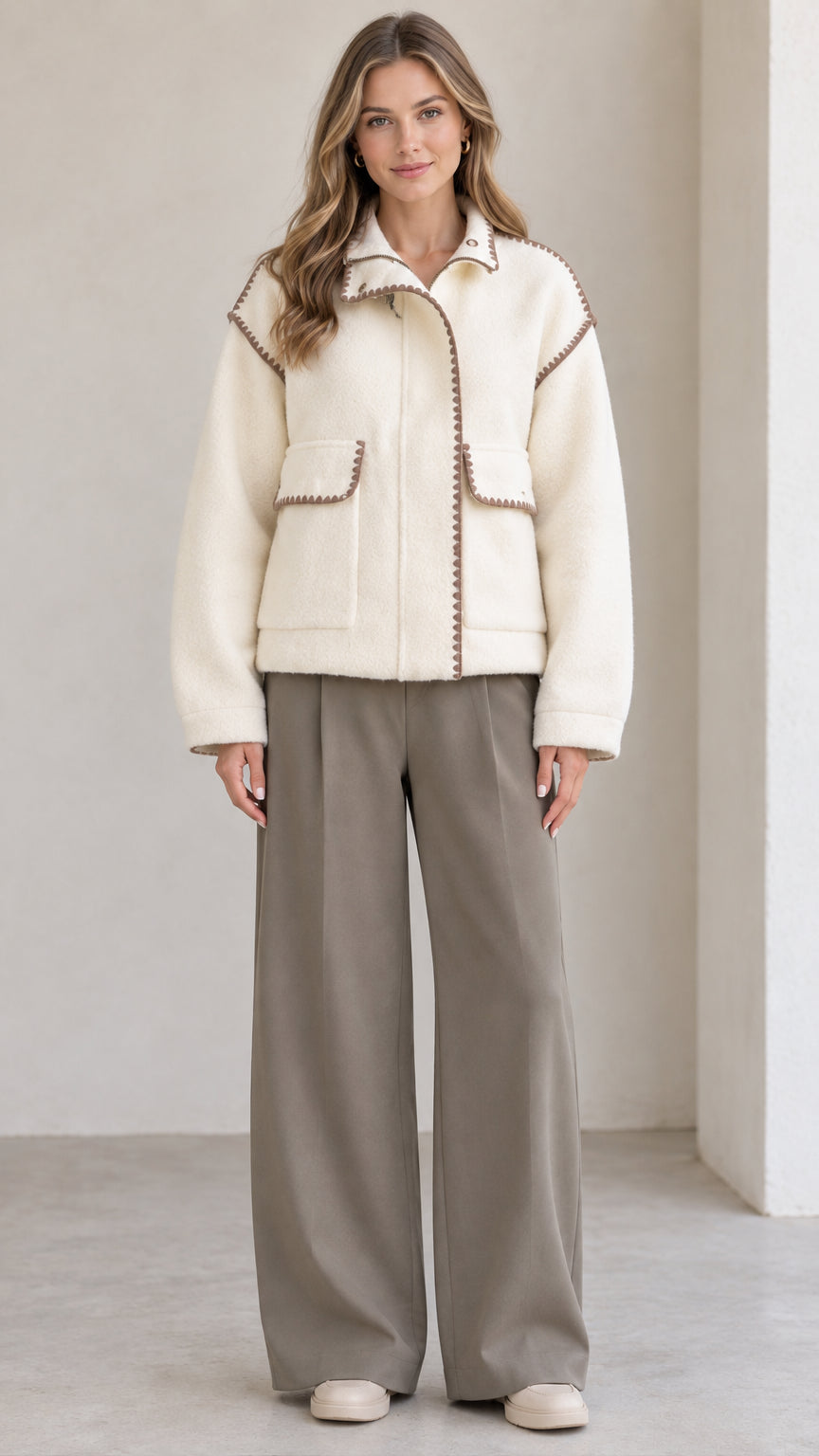 Front view of model wearing cream fleece jacket with brown blanket stitch trim and wide leg pants