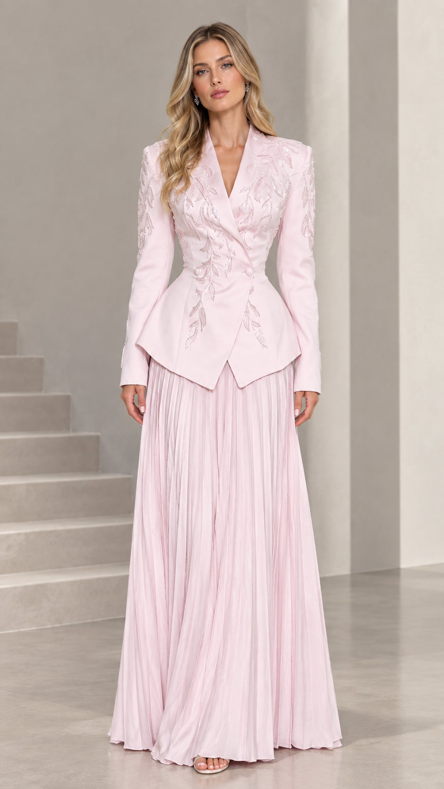 Front full-length view of woman wearing blush pink embroidered peplum blazer and pleated maxi skirt