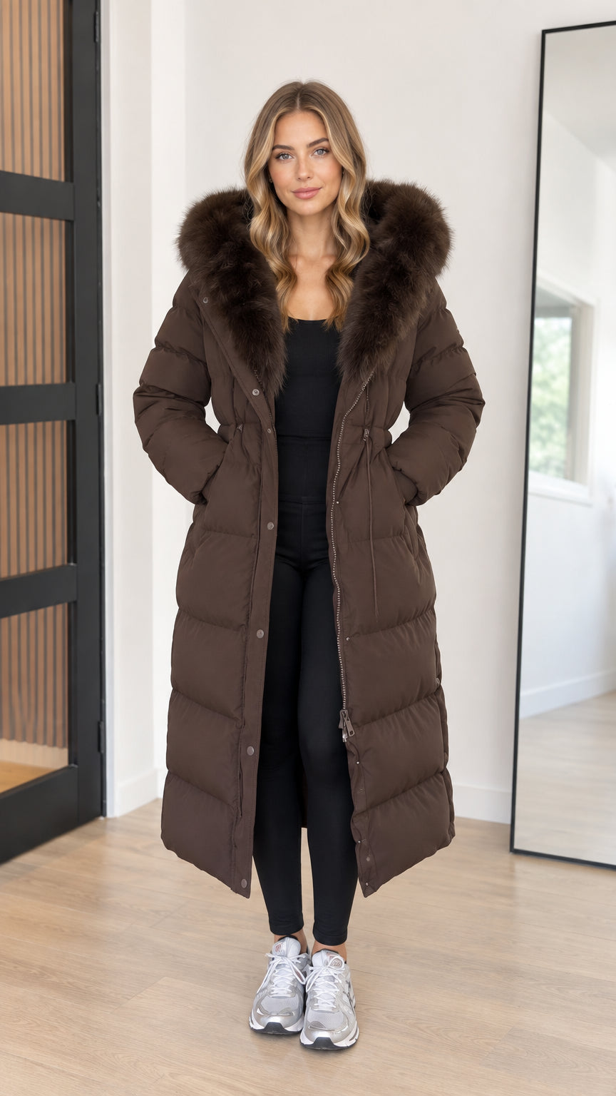 Front view of model wearing full-length brown hooded maxi puffer coat with faux fur trim