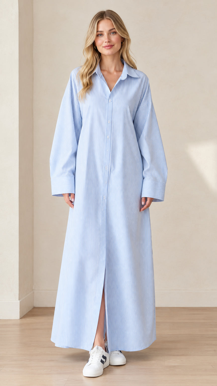 Full front view of a blonde model wearing a light blue and white striped maxi shirt dress with white sneakers