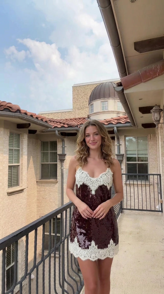 Front view of woman wearing burgundy sequin mini dress with white lace trim on outdoor balcony