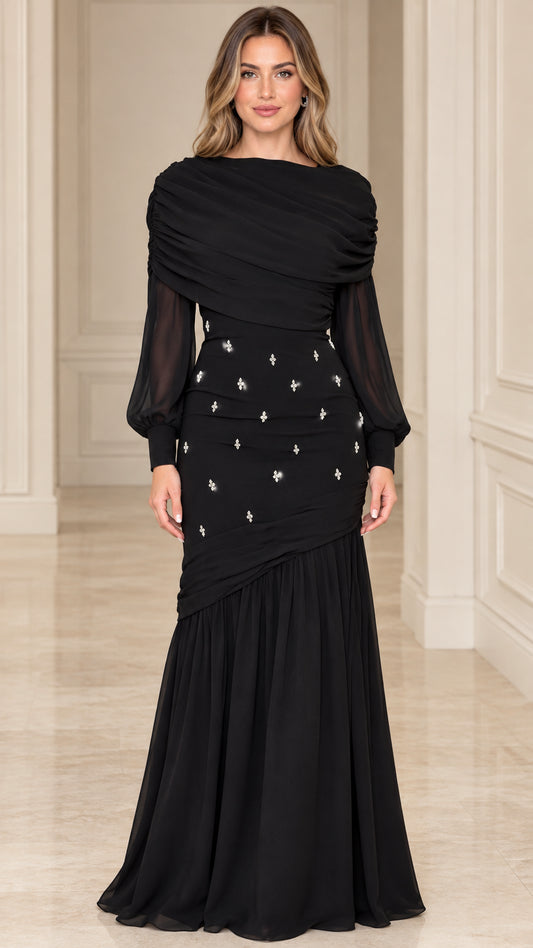 Front view of model wearing black draped cowl neck evening gown with sheer long sleeves and mermaid hem