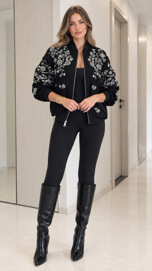 Full front view of model wearing black floral embroidered bomber jacket with black pants and boots