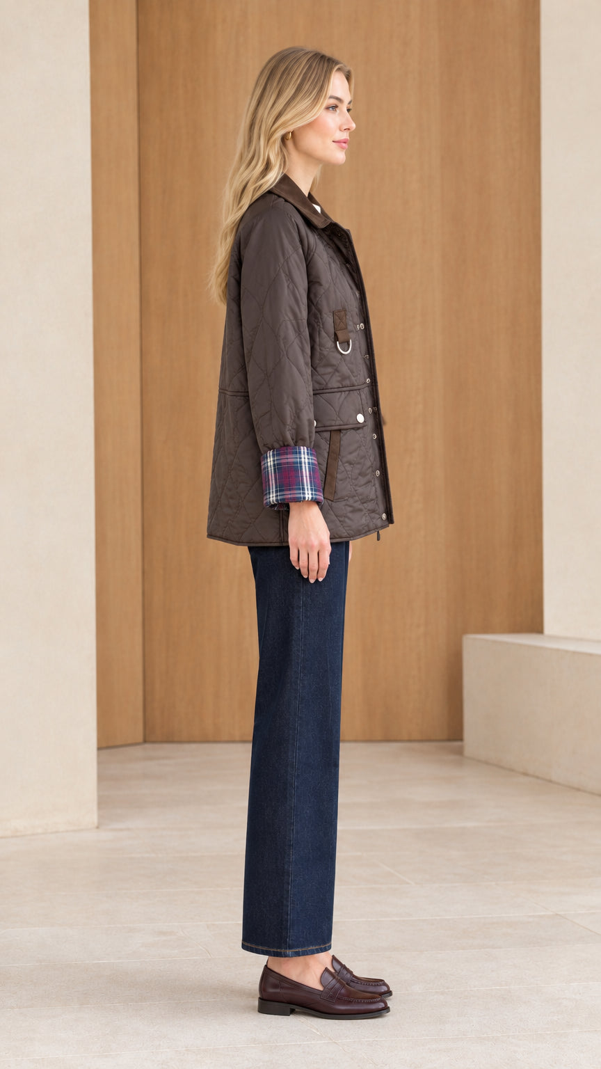 Side profile view of woman wearing dark brown quilted jacket with plaid turned cuffs