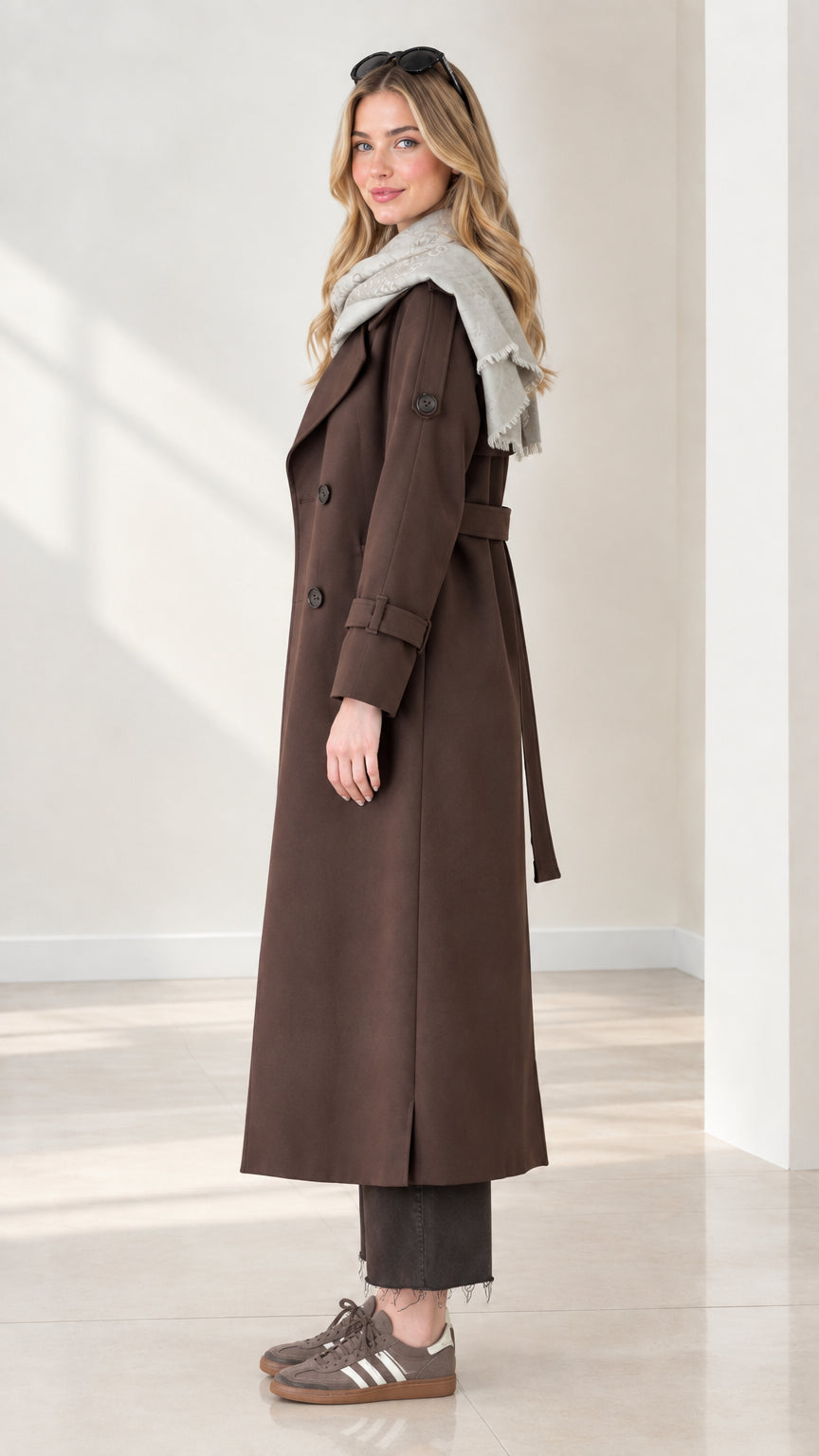 Side profile view of model in full-length chocolate brown trench coat with belt
