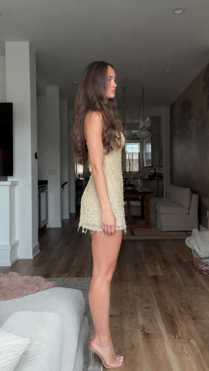 Side profile of model wearing champagne gold sequin fringe mini dress