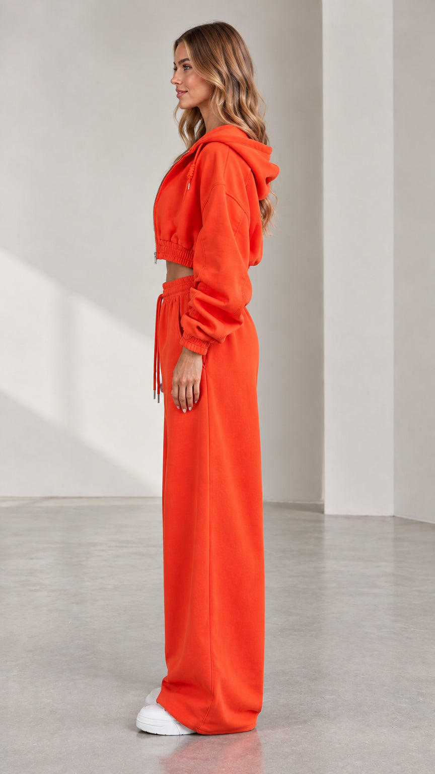 Side profile of woman wearing orange two-piece cropped hoodie and wide leg pants tracksuit