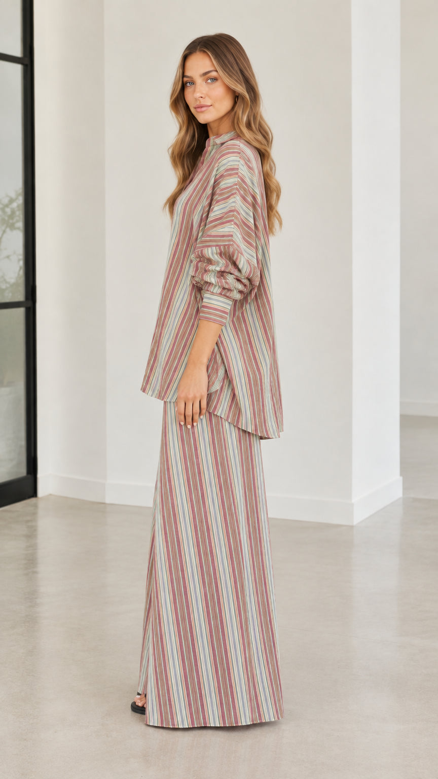 Side angle view of model in rust multi-color vertical striped two-piece pant set