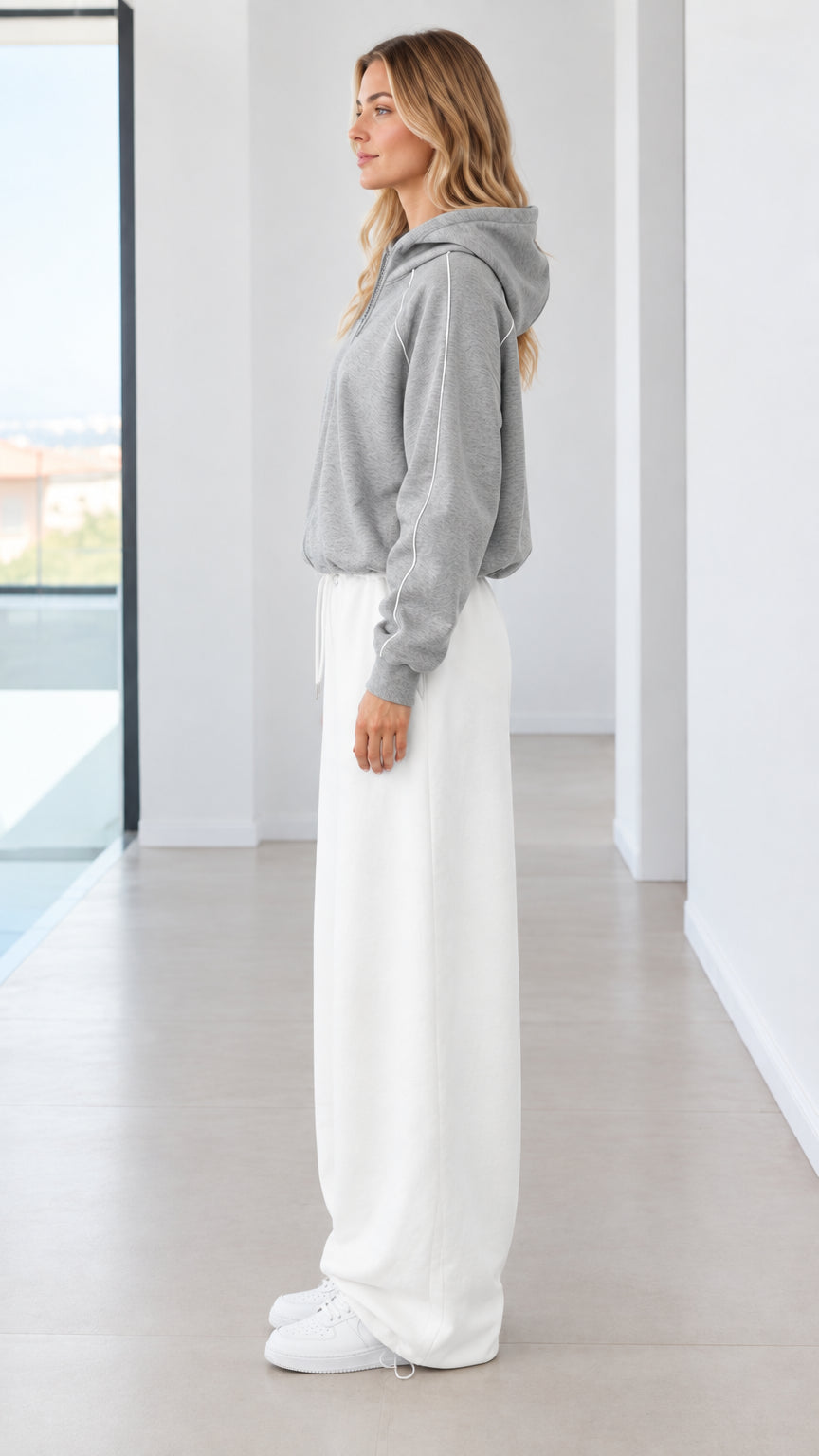 Side profile of model in heather grey hooded sweatshirt and white wide-leg sweatpants