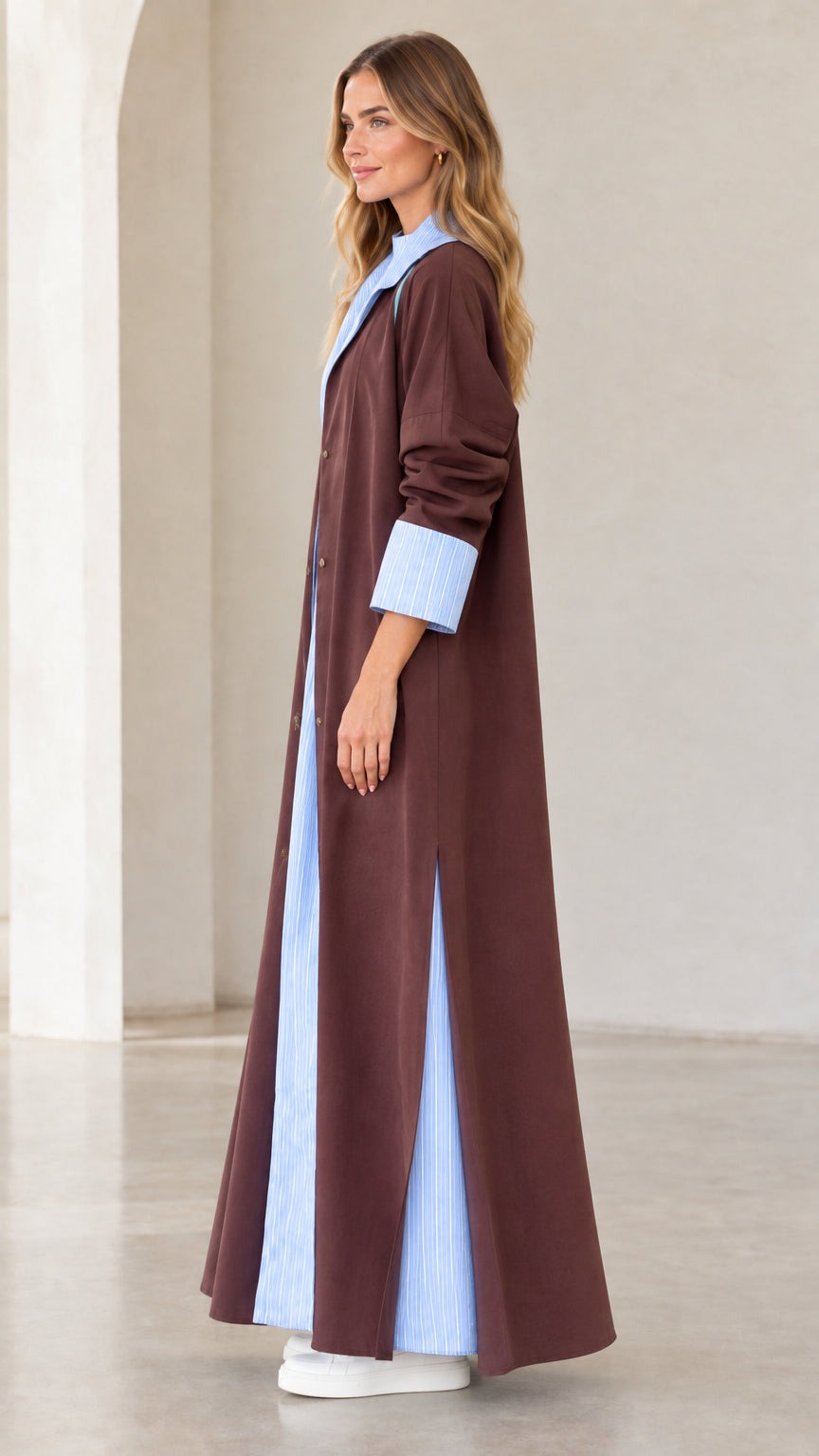 Side profile view of women's brown maxi duster coat featuring side slit and contrast hem detail