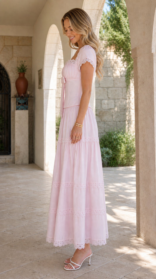 Side full-length view of model wearing a blush pink romantic tiered maxi dress in an outdoor courtyard