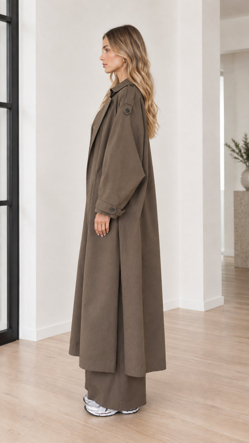 Side profile of woman in long olive brown trench coat and wide-leg trousers