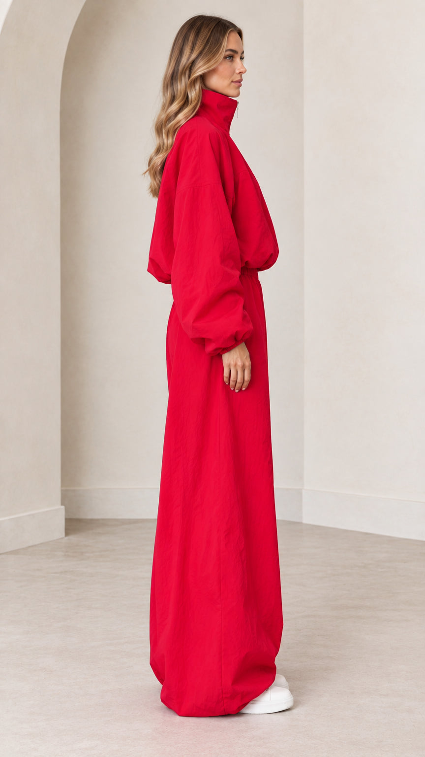 Side profile view of red long-sleeve parachute jumpsuit with elastic waist
