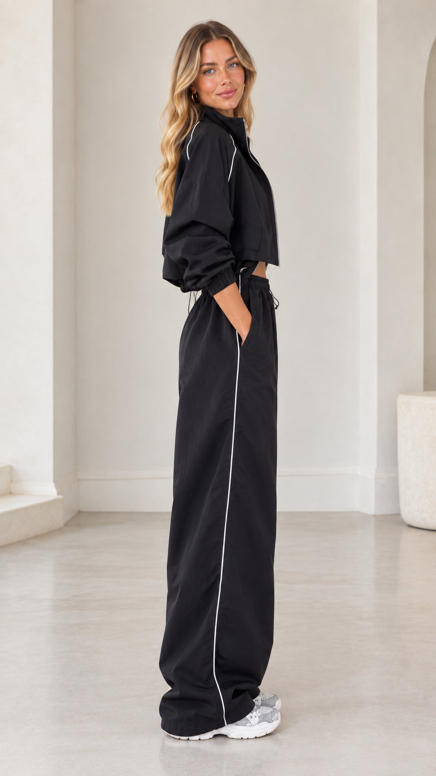 Side profile view of black cropped track jacket and matching side-piped wide leg pants