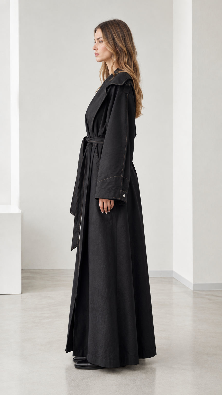 Side profile view of woman wearing long black belted trench coat