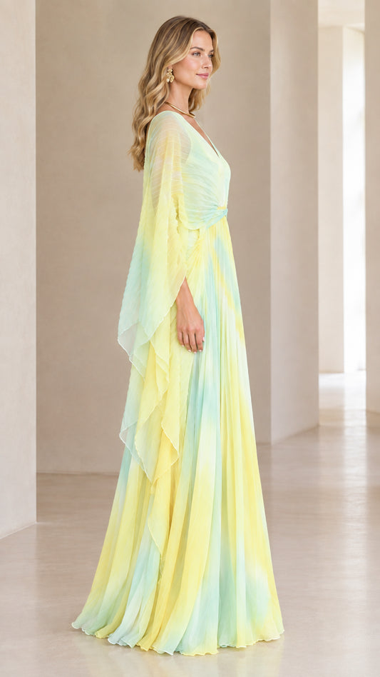 Side angle of woman in flowing yellow ombre pleated formal gown with cape sleeves