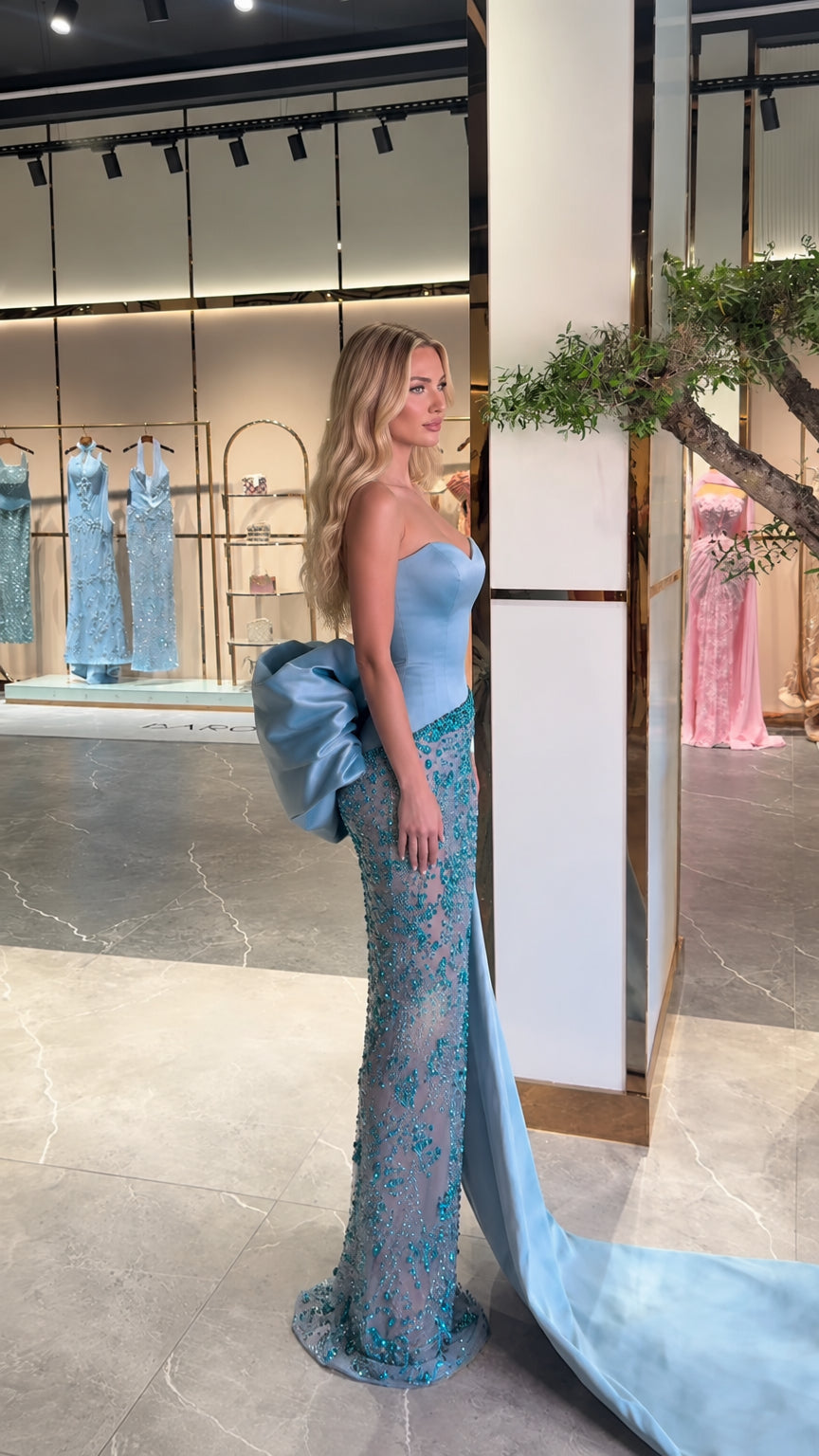 Side profile of sky blue crystal beaded formal dress showing oversized satin bow and train
