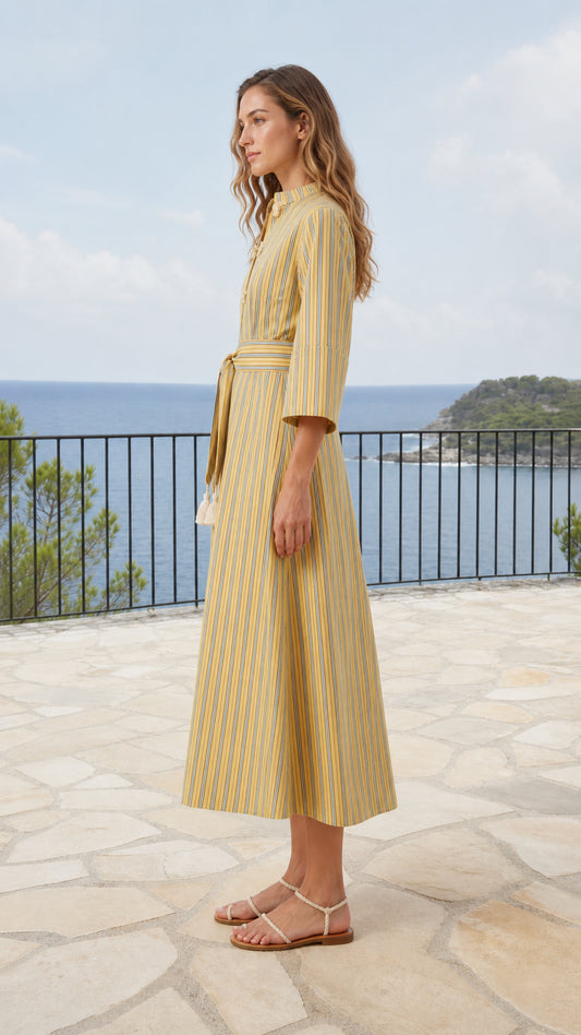 Side profile of model wearing yellow striped A-line midi dress on seaside balcony