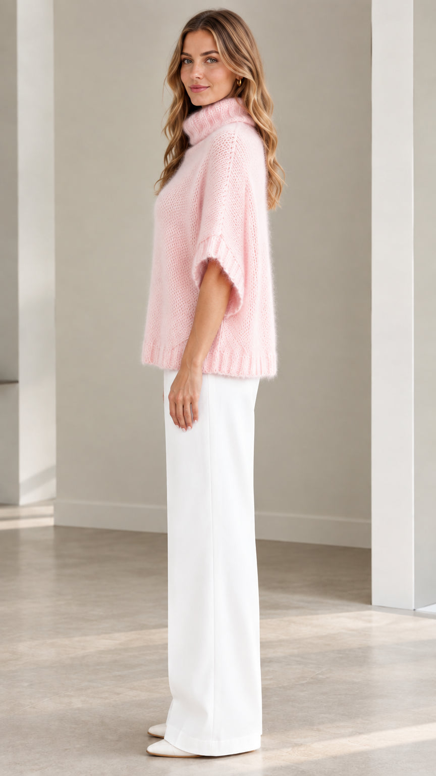 Side profile of model wearing Light Pink turtleneck poncho knit sweater