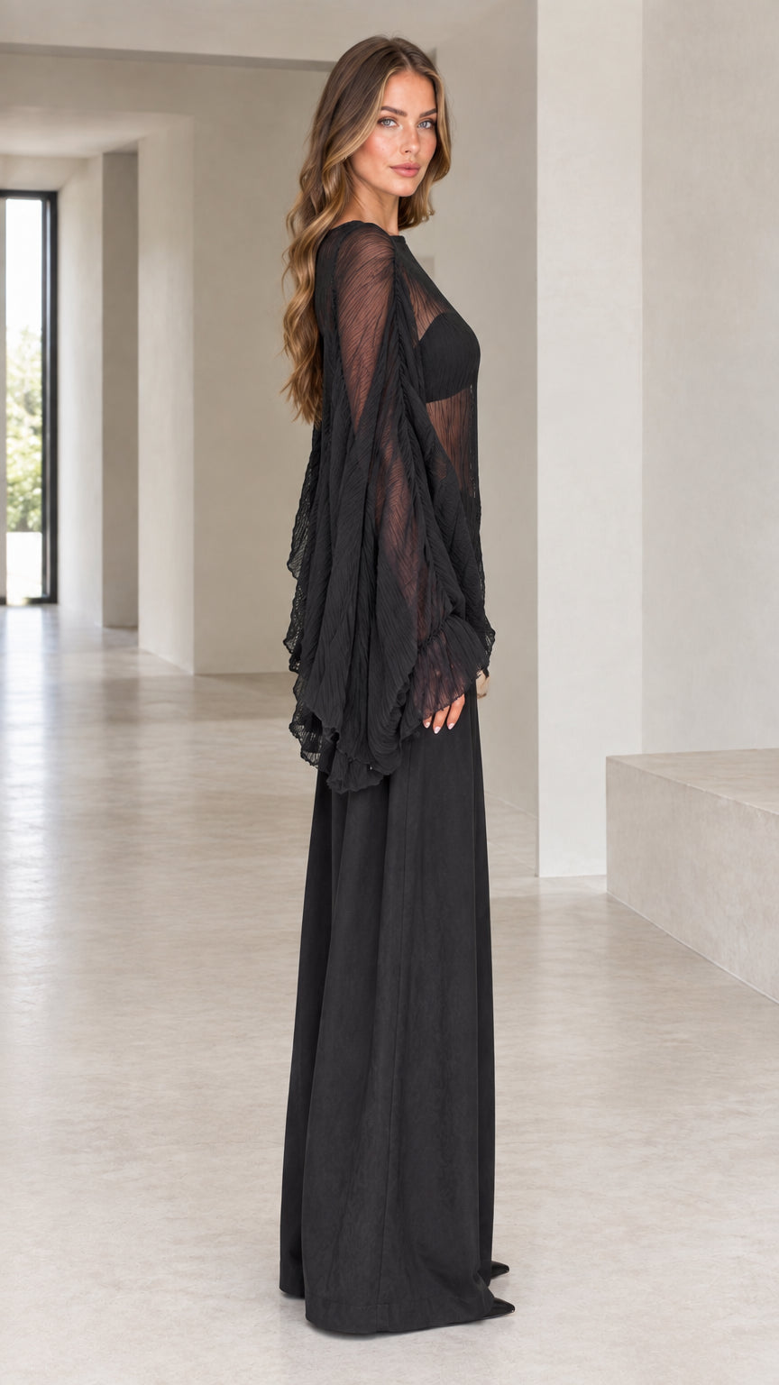 Side profile of woman wearing black sheer pleated bell sleeve top with matching palazzo pants