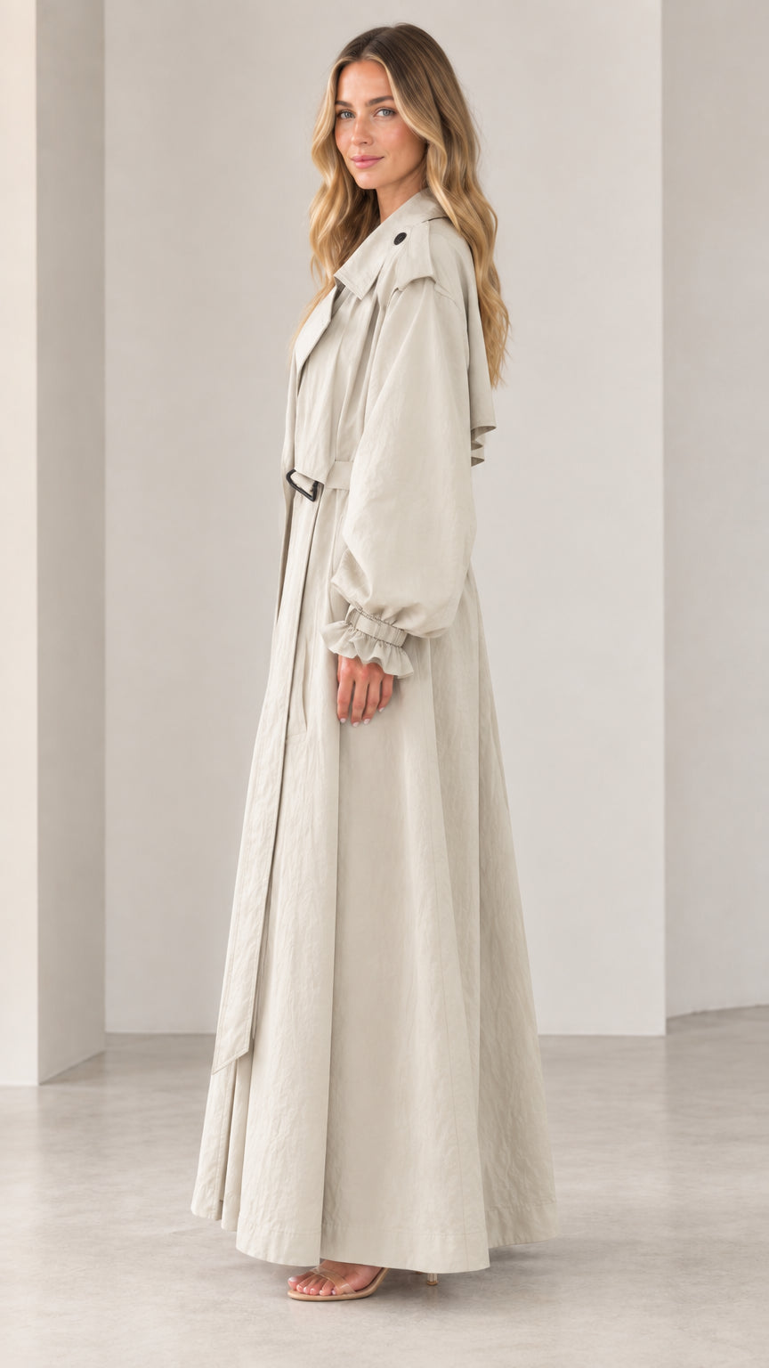 Side 3/4 view of elegant beige maxi trench coat showing dramatic sweeping hem