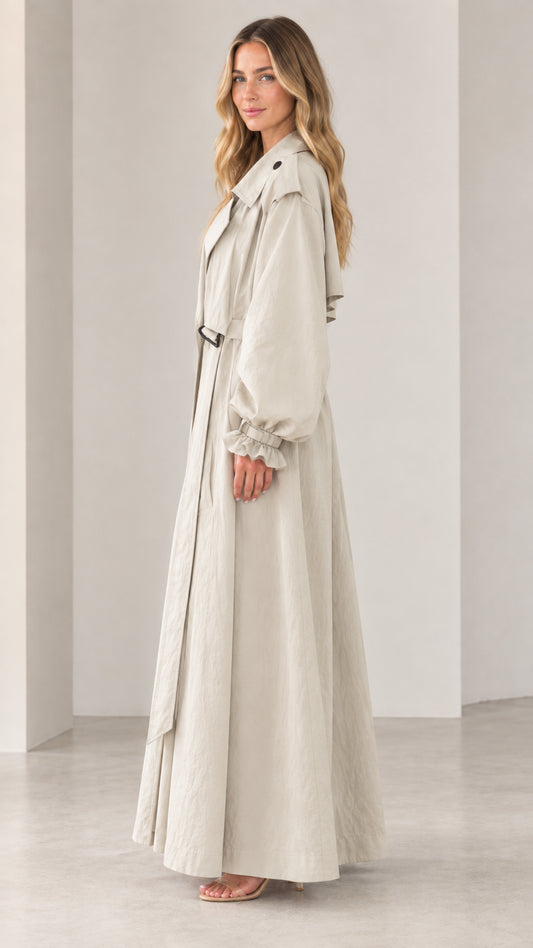 Side 3/4 view of elegant beige maxi trench coat showing dramatic sweeping hem