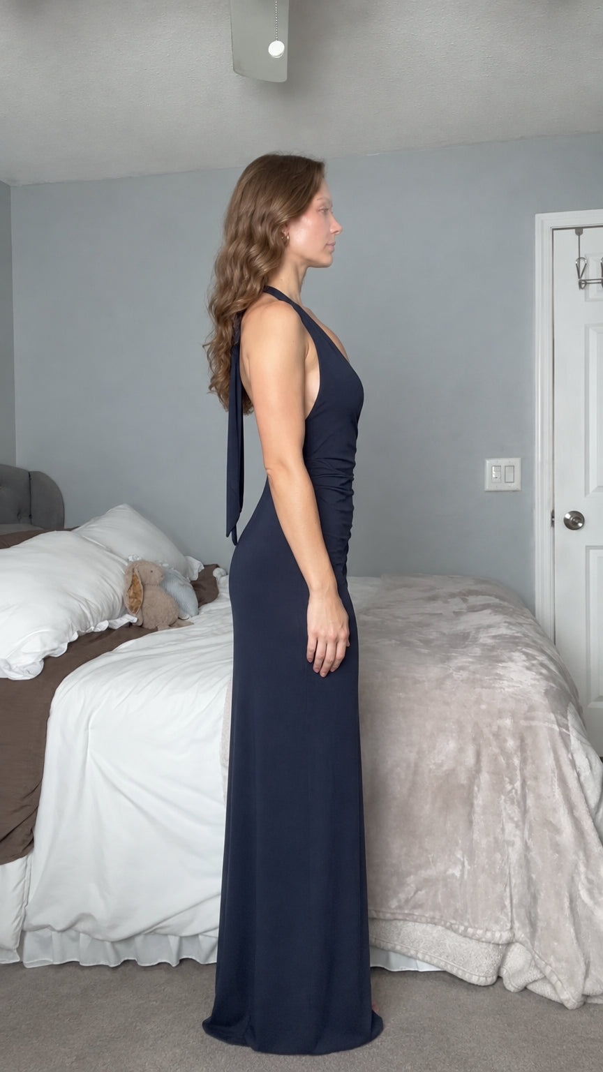 Side profile view of woman wearing navy blue sleeveless open back evening maxi dress