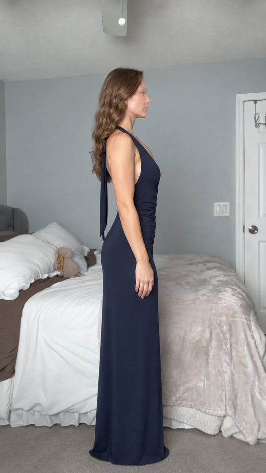 Side profile view of woman wearing navy blue sleeveless open back evening maxi dress