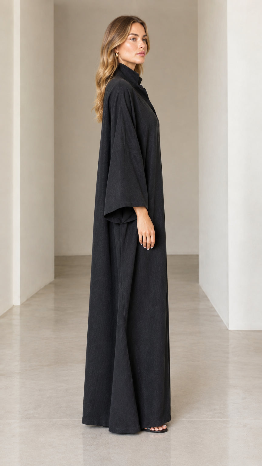 Side view of woman wearing flowing black full-length kaftan with wide sleeves
