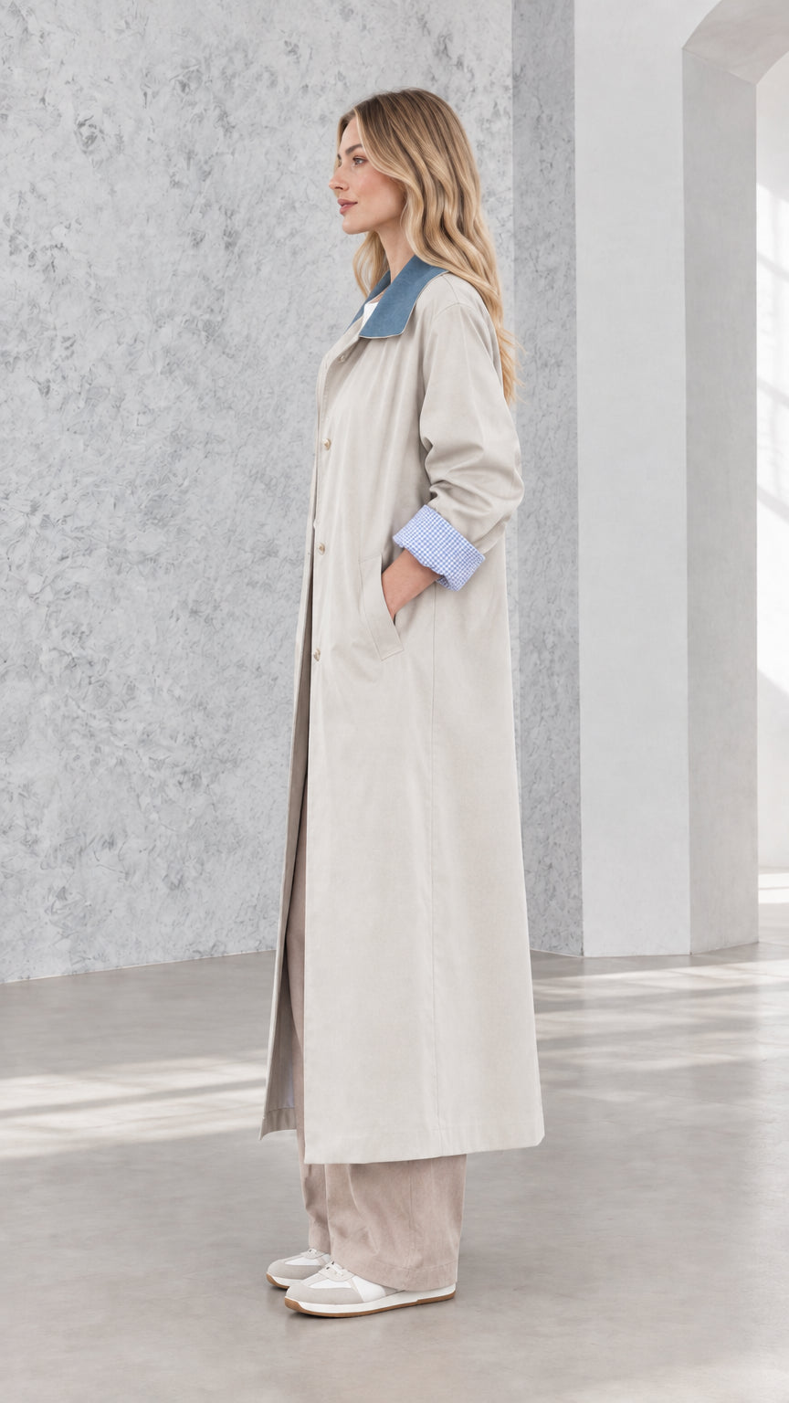 Side profile of woman in full-length light grey duster coat with blue contrast collar