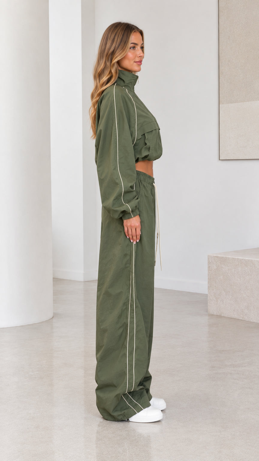 Side profile view of model in olive green tracksuit set showing piping detail
