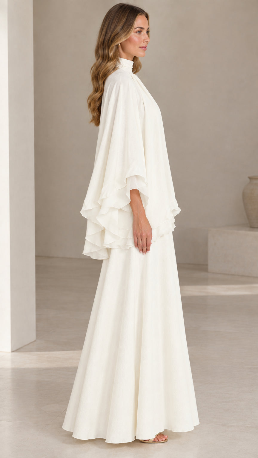 Side profile of model wearing ivory white tiered capelet evening maxi dress
