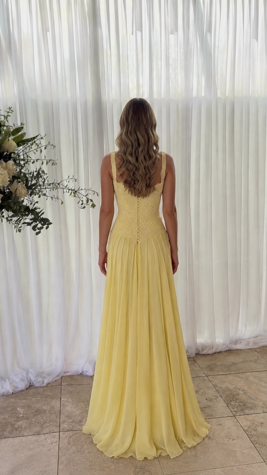 Back view of model wearing yellow chiffon gown showing button-down back detail