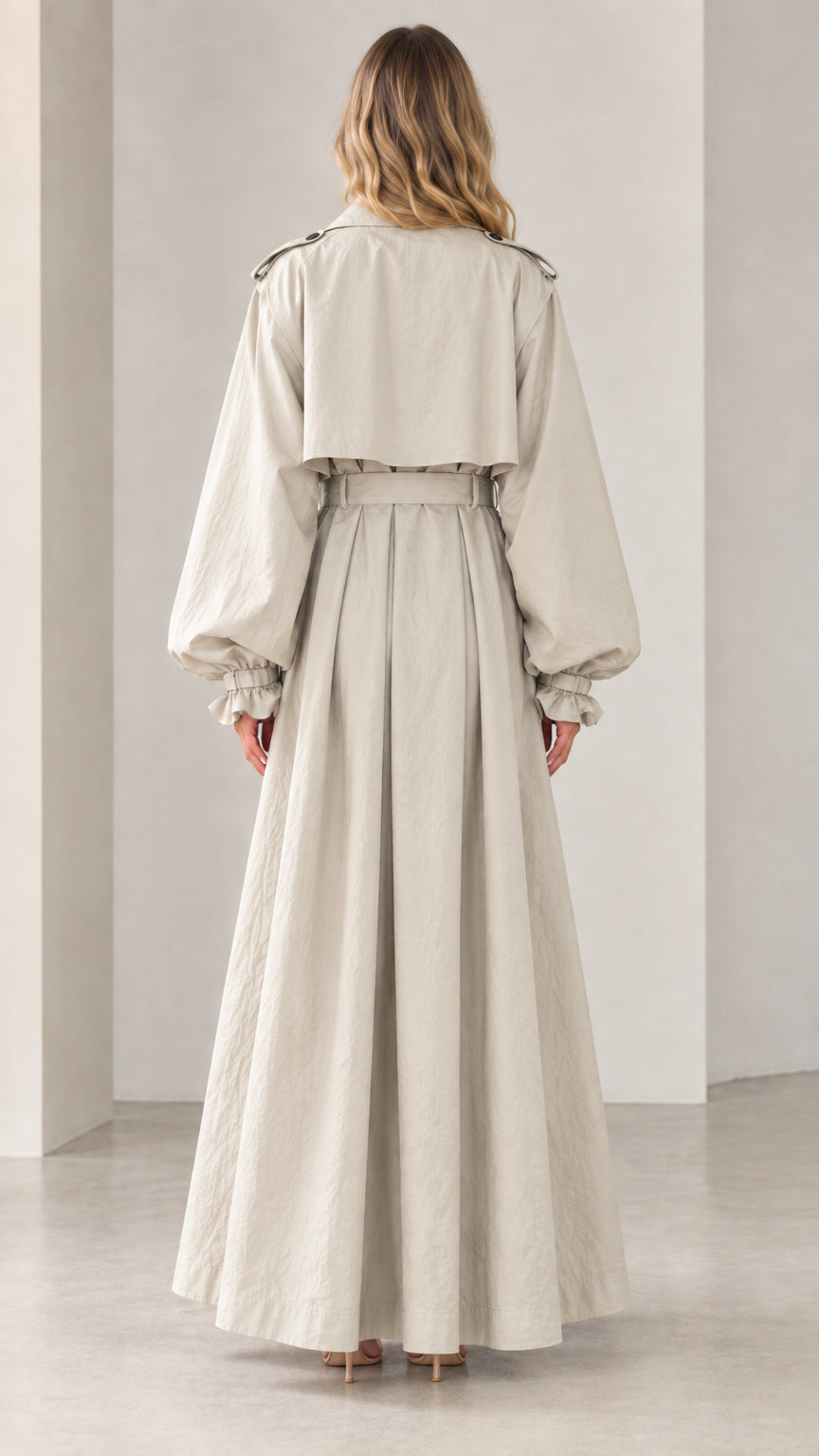 Full back view of beige maxi trench coat highlighting storm flap and flared skirt
