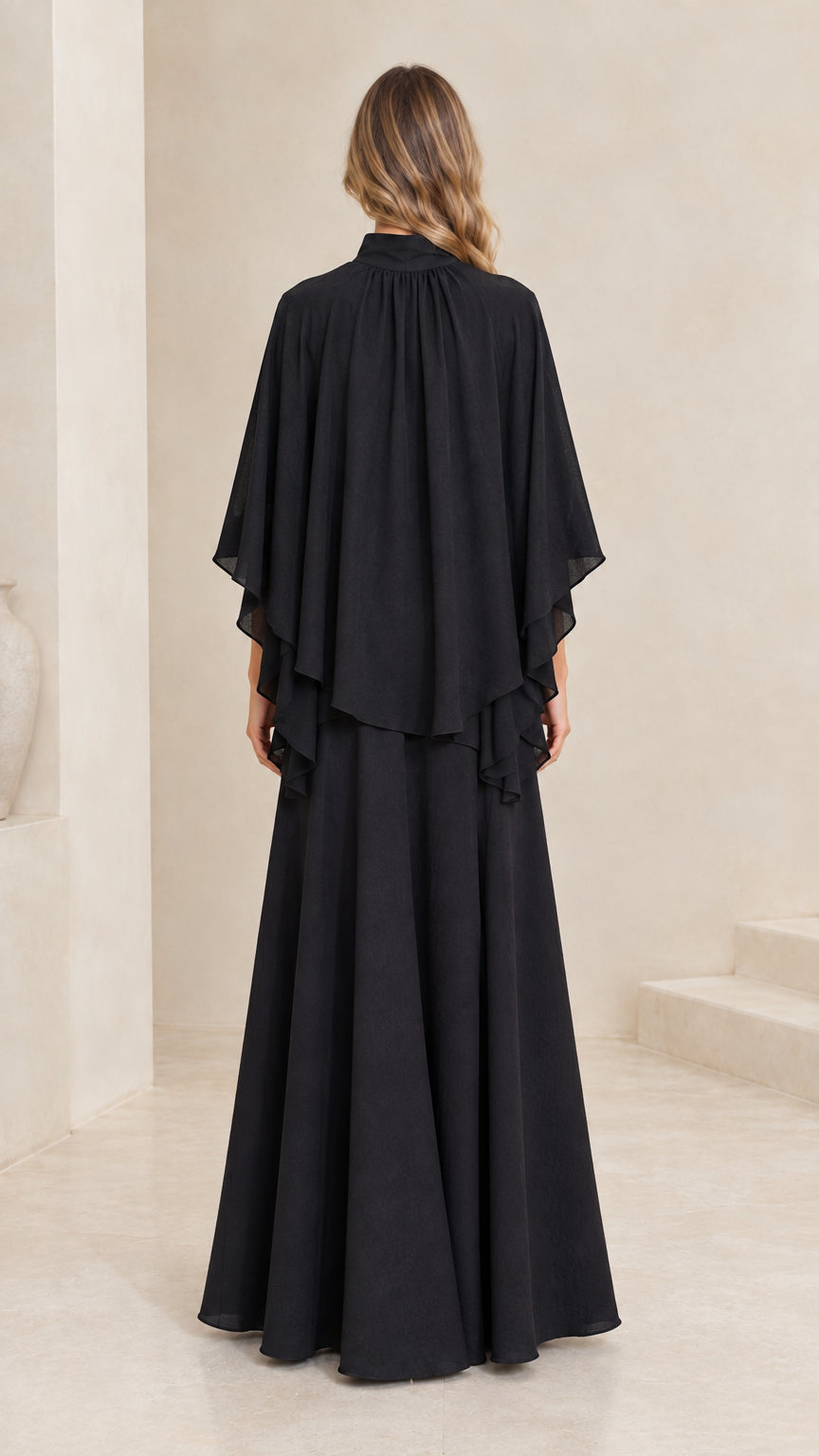 Back view of model in full-length black capelet dress
