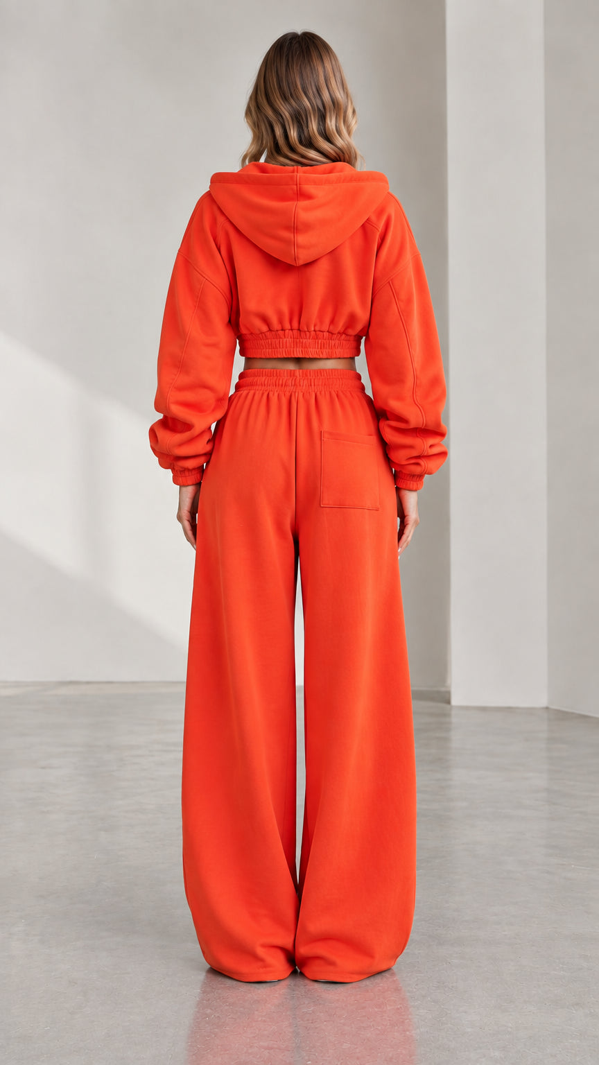 Back view of woman wearing orange hooded cropped jacket and relaxed wide leg sweatpants