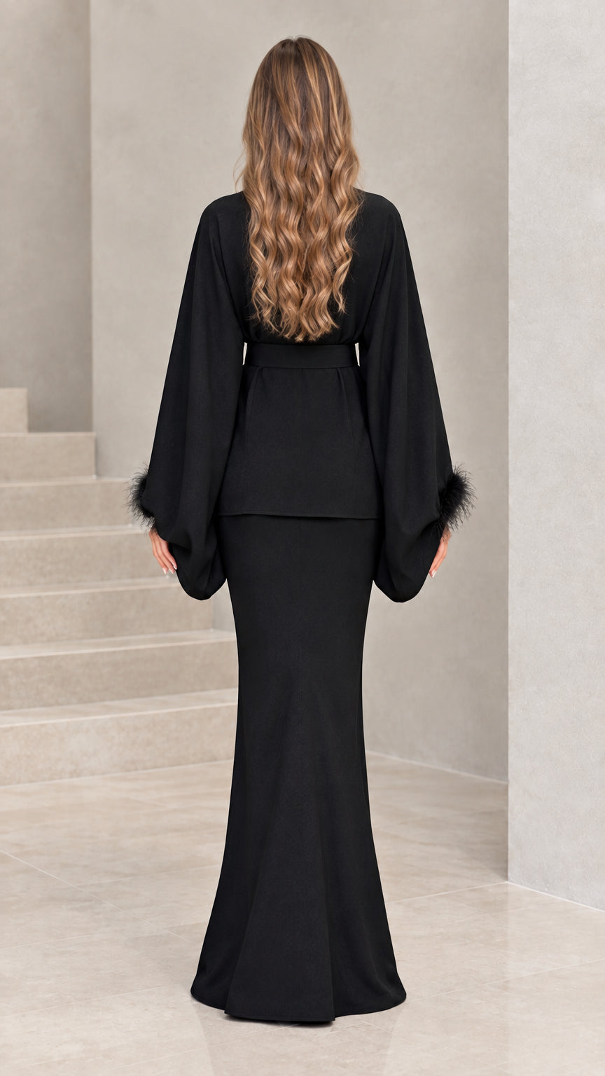 Back view of model in black long-sleeve belted tunic top and fluted maxi skirt