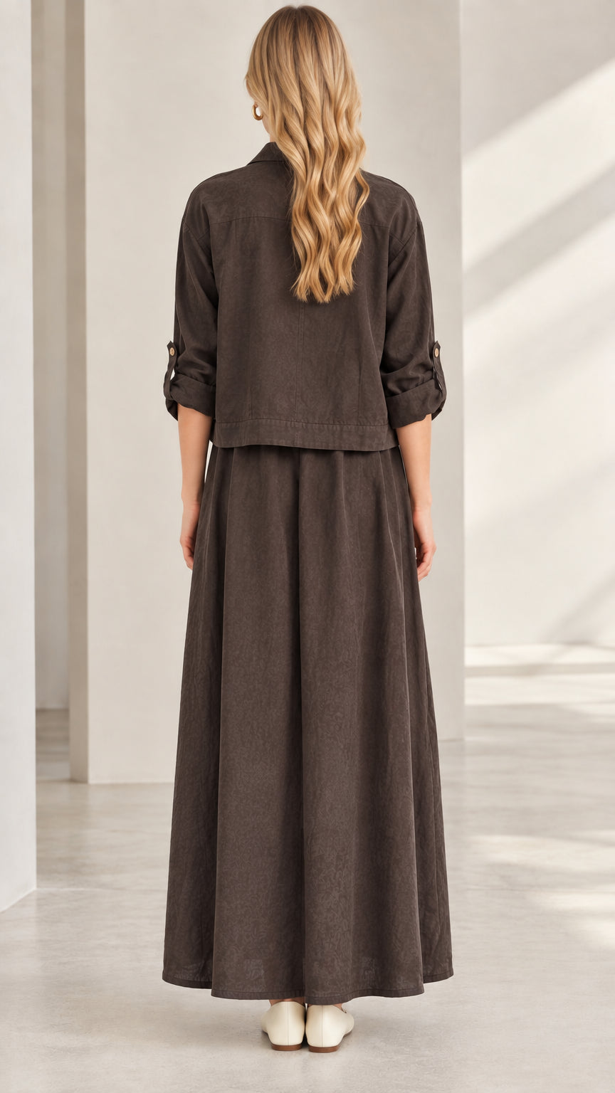 Rear view of model wearing dark brown long sleeve jacket and pleated maxi skirt